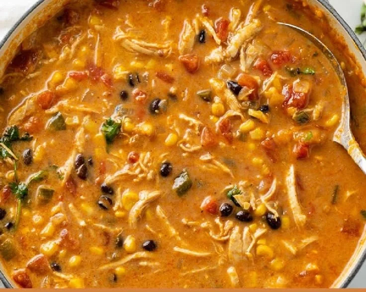 Bowl of creamy chicken tortilla soup garnished with tortillas and herbs.